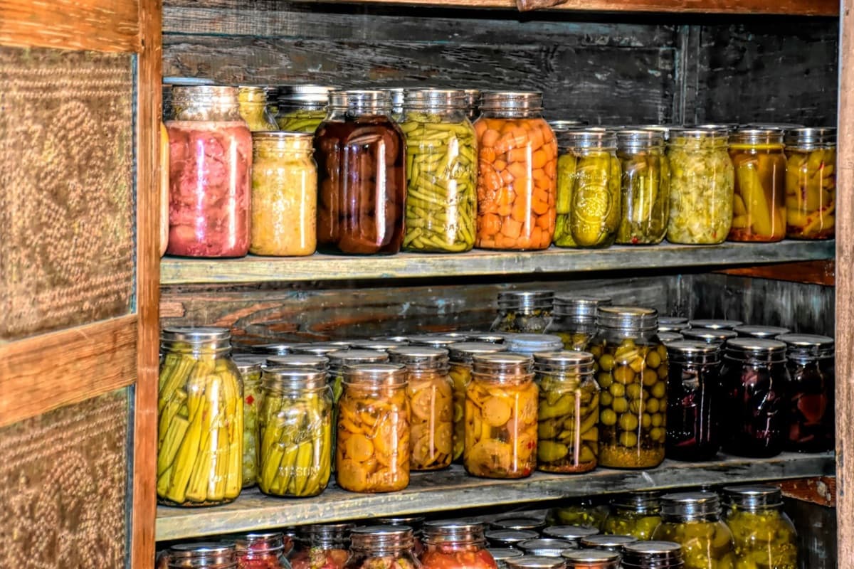 Rustic wooden pantry shelves lined with rows of home-canned jars of preserved vegetables, pickles and jams