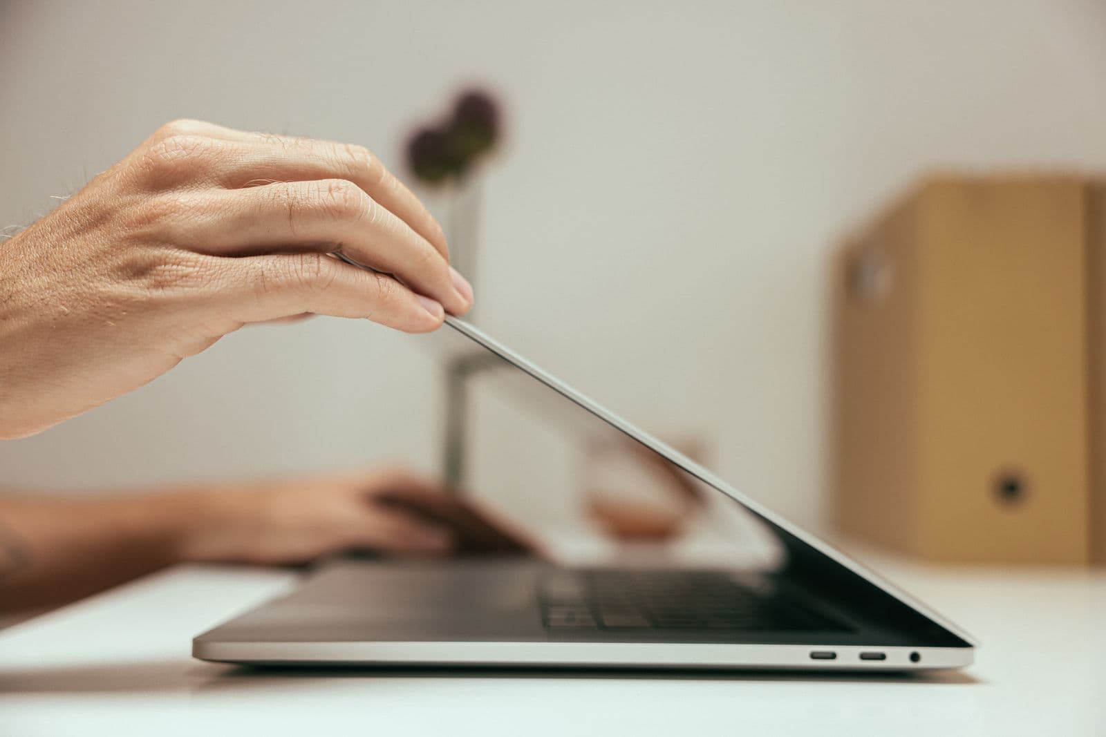 A close-up of a hand closing a laptop lid on a clean, minimal desk